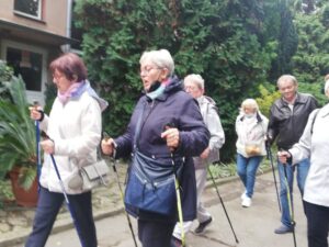 grupa osób spaceruje z kijkami na łonie natury - zajęcia taneczno-ruchowe w Klubie Seniora