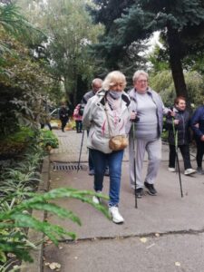 grupa osób spaceruje z kijkami na łonie natury - zajęcia taneczno-ruchowe w Klubie Seniora
