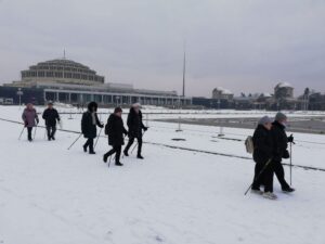 idąca po śniegu z kijkami grupa ludzi na tle w oddali Hala Stulecia - zajęcia taneczno-ruchowe w Klubie seniora