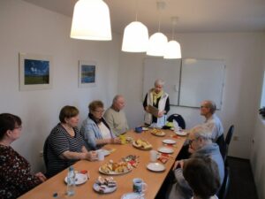 grupa osób siedzących przy stole przy kawie i herbacie, na stole po środku jest ciasto - Spotkanie z wolontariuszami w Kole Zgorzelec