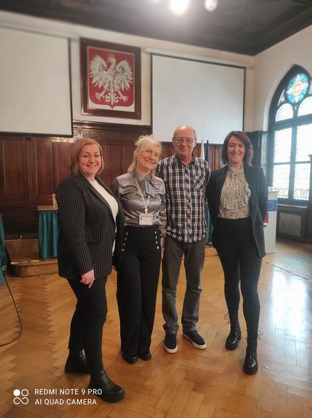Jeden mężczyzna i 3 kobiety pozują do zdjęcia stojąc w sali. Za nimi widać godło Polski