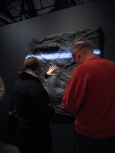 dwie osoby w pozycji stojącej dotykają skały, która jest podświetlona lampą - członkowie Koła Wałbrzych w galerii BWA