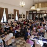 sala wypełniona ludźmi siedzącymi przy stołach pokazana z podwyższenia